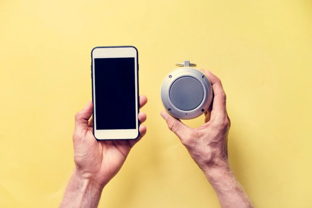 hands holding smartphone and bluetooth speaker
