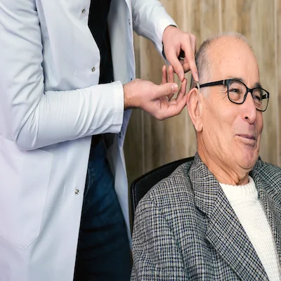 A man smiling while being fitted for hearing aids by a doctor.