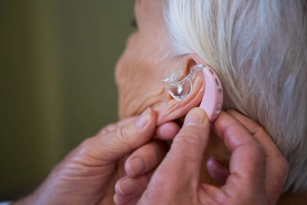 doctor inserting hearing aid in senior patient ear