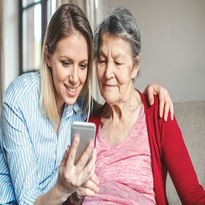 Younger woman puts her arm around her mother while both smile looking at smartphone screen.