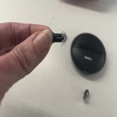 A woman holds a small Eargo 7 hearing aid in her thumb and forefinger to demonstrate the device’s size