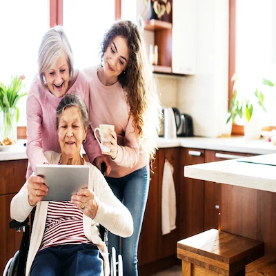 Two women lean over the shoulder of an older woman who is looking at an iPad.