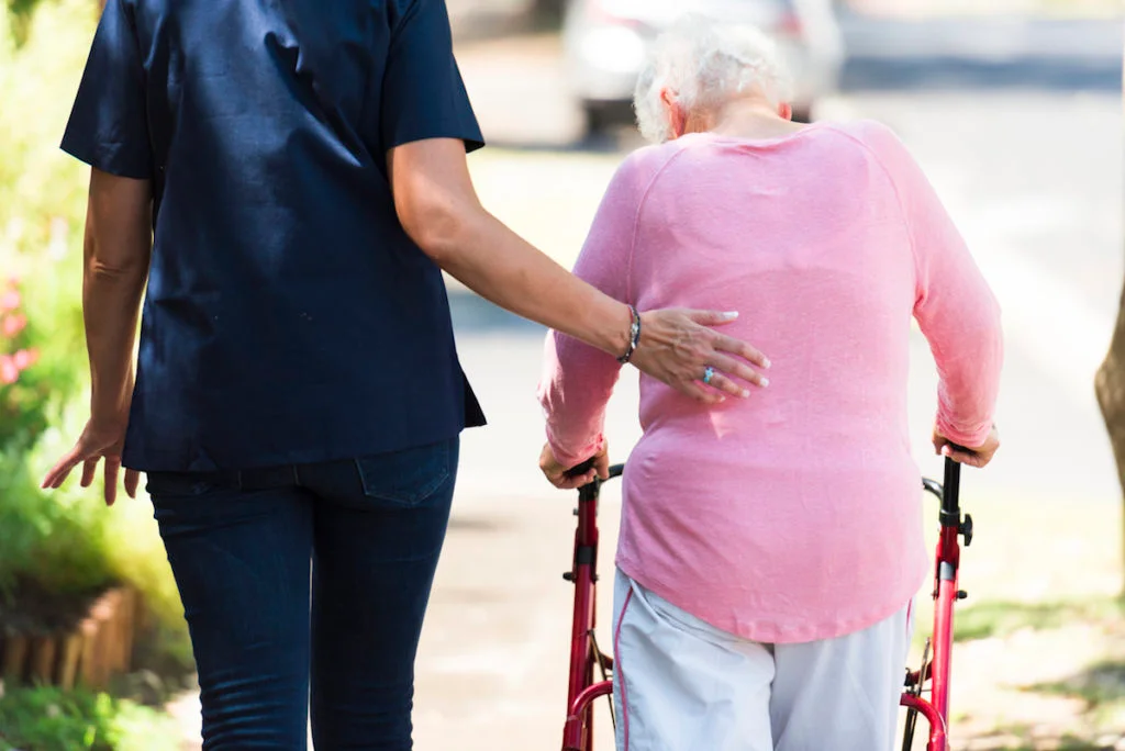 Caregiver helping an elderly woman with her walking aid outdoors in the grounds of the retirement home