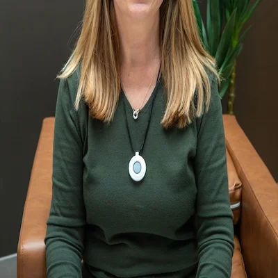 Woman in green sweater wears medical alert necklace around her neck while sitting down