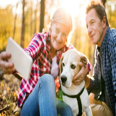 A woman takes a picture of herself, a man, and a dog using her phone.