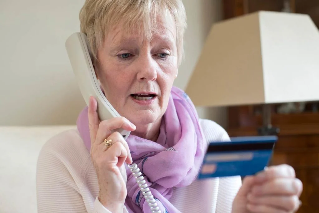 elderly woman holding credit card on phone scam