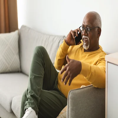 Older adult man sits on the couch and talks on the phone while smiling