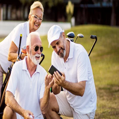A group of older adults wearing white smile while looking at a phone on the golf course