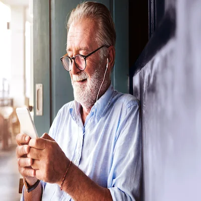 Older man smiles while wearing headphones plugged into his phone